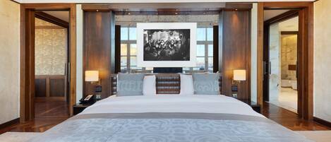 A large bed with a patterned bedspread, two bedside tables with lamps, a large framed picture above the bed, and wooden paneling on the walls.