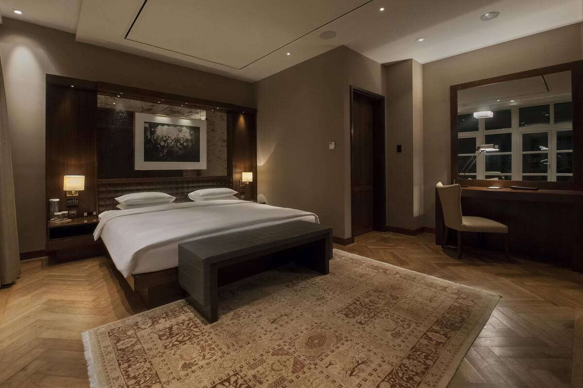 Una habitación de hotel moderna con una cama grande, mesitas de noche con lámparas, un escritorio con una silla y un espejo grande.