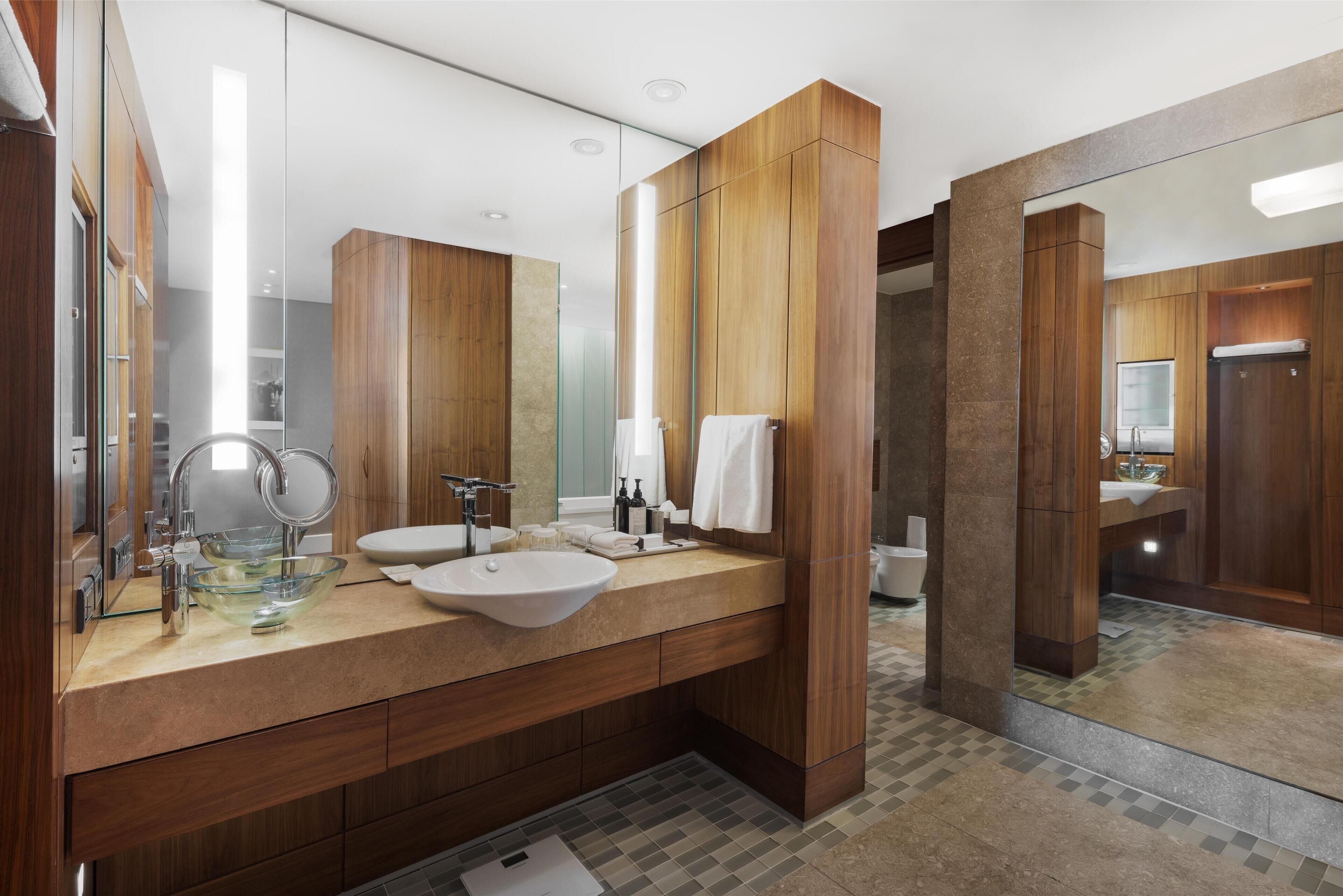 Un baño moderno con muebles de madera, un lavabo de vidrio y un espejo grande.