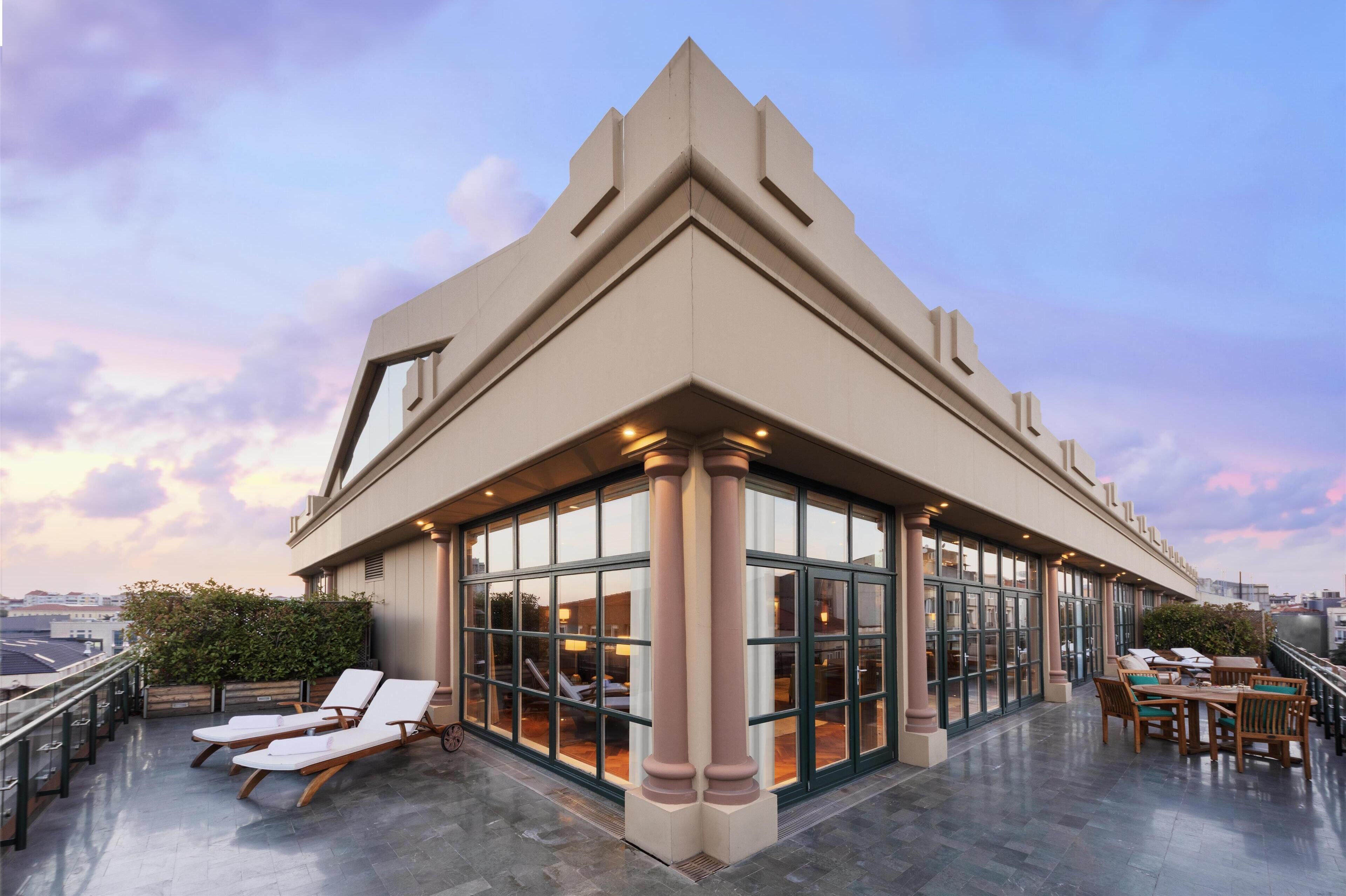 A modern building with large glass windows and a rooftop terrace with lounge chairs and tables.