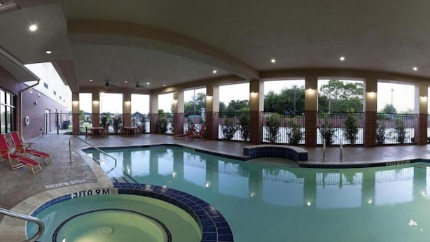 An indoor swimming pool with a 3FT9M depth marker, surrounded by a covered area with seating and a view of the outdoors.