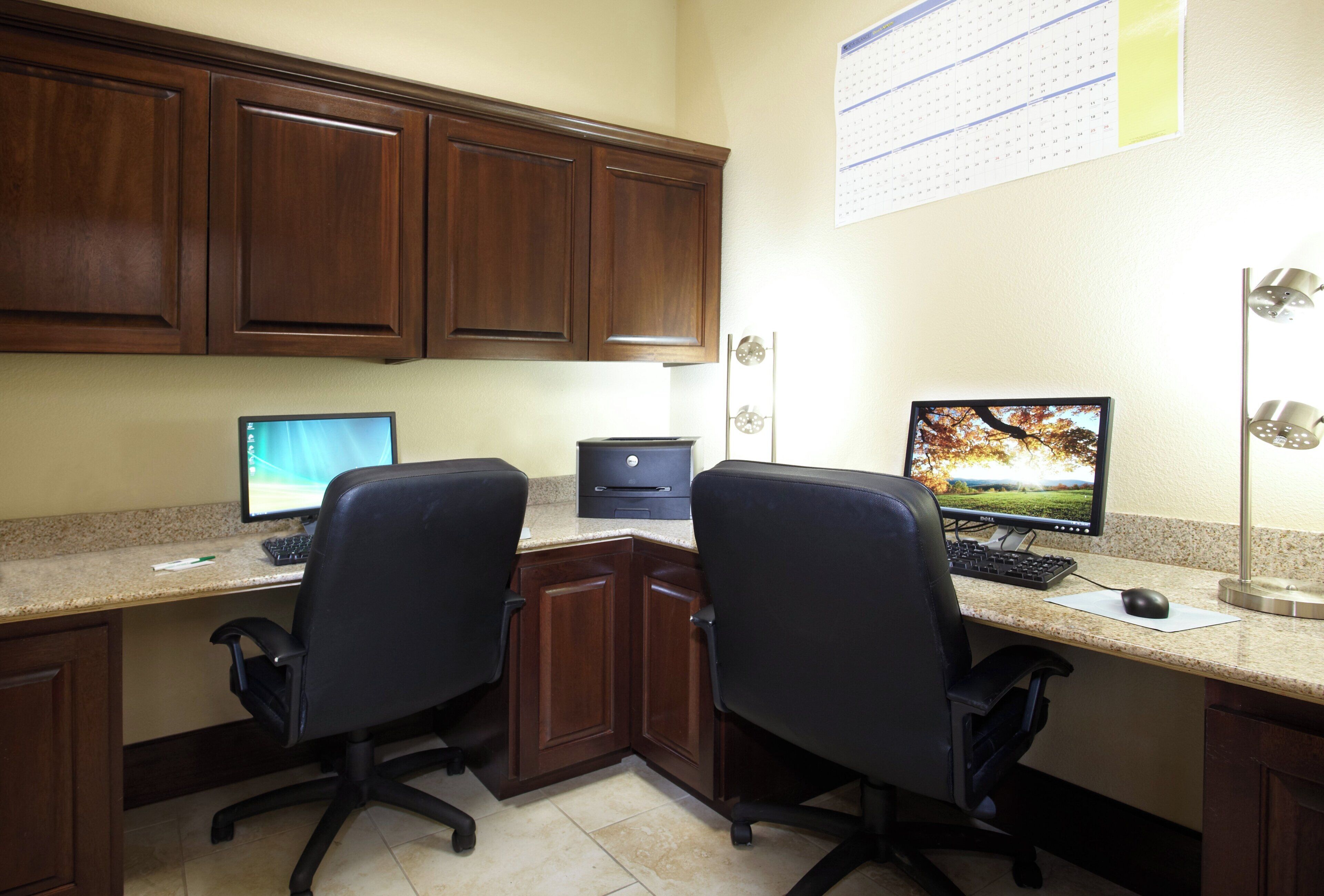 A workspace with two desks, each with a computer and keyboard, two office chairs, a printer, and a calendar on the wall.