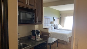 A compact hotel room with a kitchenette, including a microwave, coffee maker, and sink. The room features a bed with white linens and a window with curtains. - Holiday Inn Express & Suites Silt-Rifle by IHG (Silt)