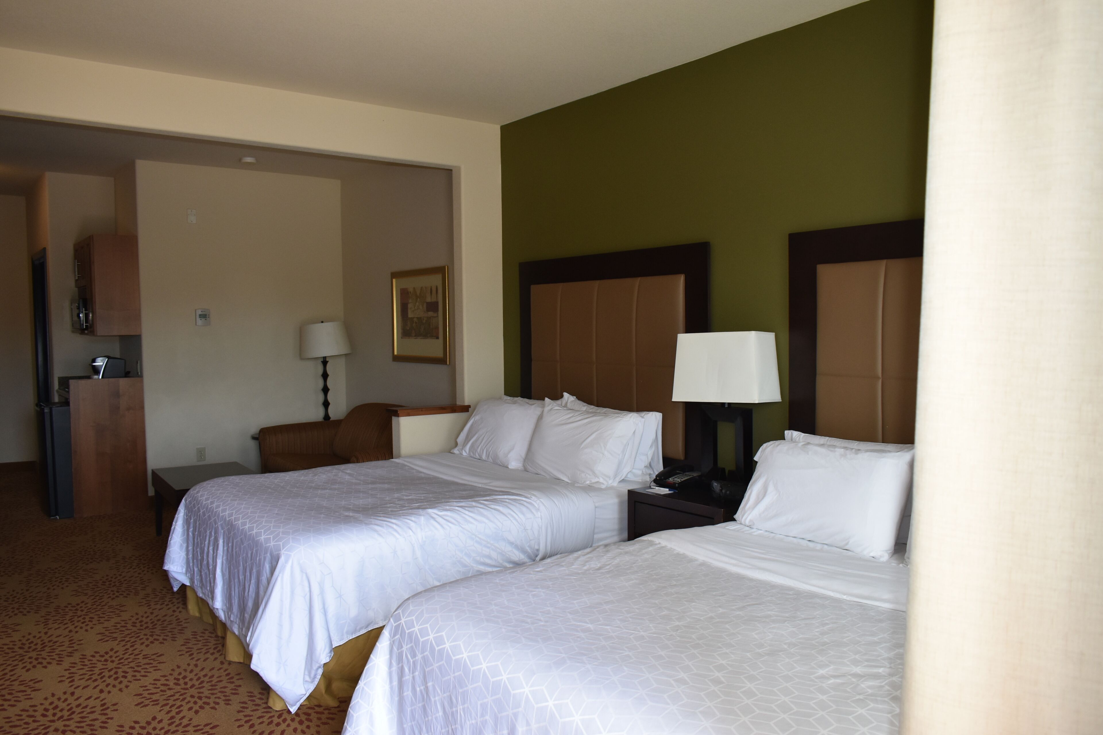 Quarto de hotel com duas camas, uma escrivaninha, uma cadeira, um abajur e um quadro na parede.