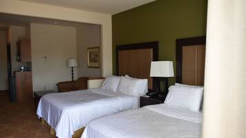 Quarto de hotel com duas camas, uma escrivaninha, uma cadeira, um abajur e um quadro na parede.