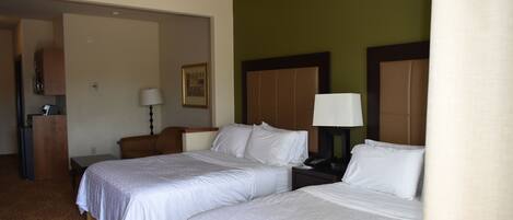 Quarto de hotel com duas camas, uma escrivaninha, uma cadeira, um abajur e um quadro na parede.