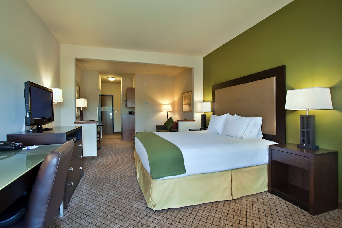 Ein Hotelzimmer mit Bett, Schreibtisch, Stuhl, Fernseher, Lampen und einem kleinen Tisch.