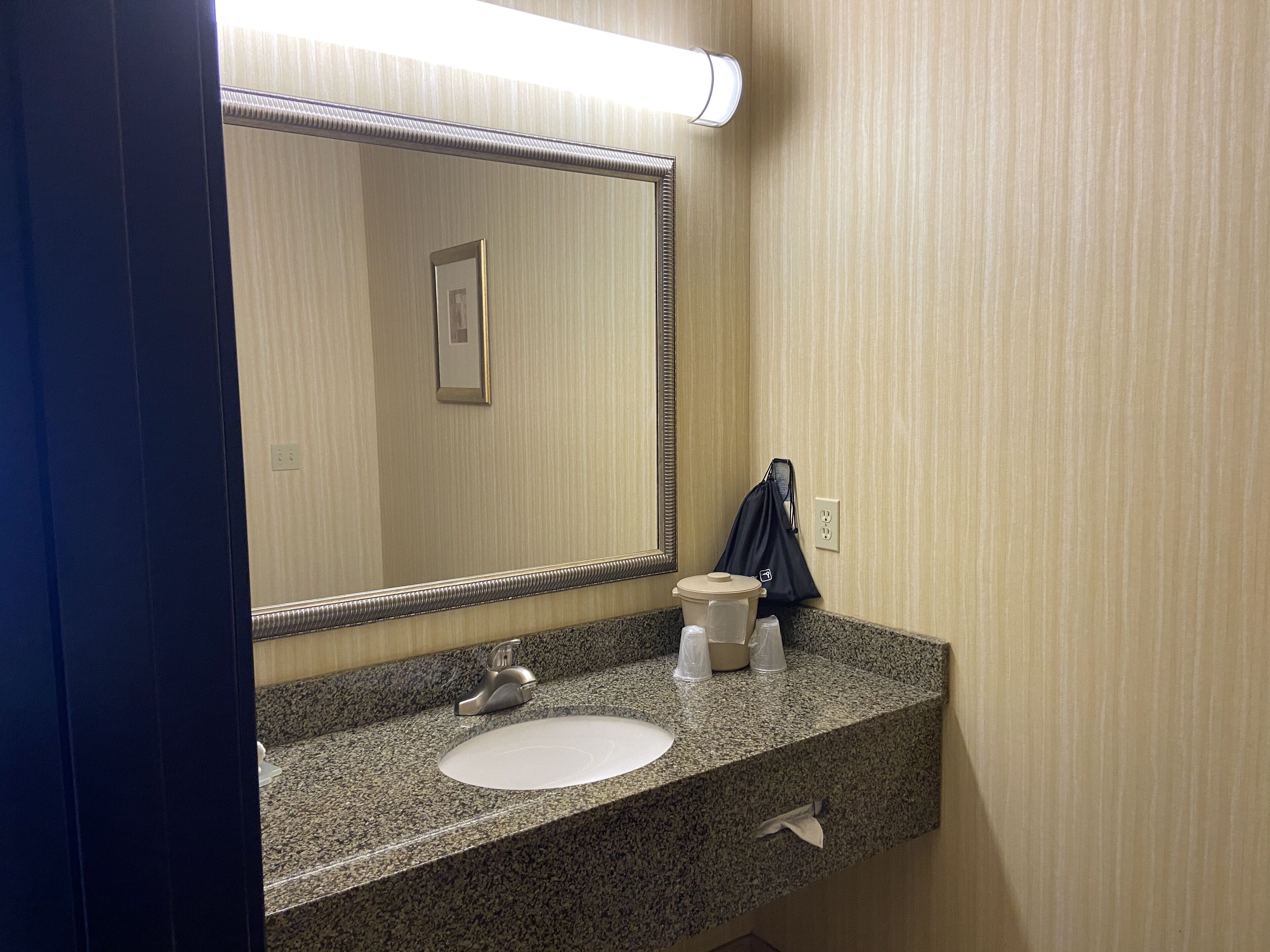 A bathroom with a granite countertop, a sink, a mirror, and a towel dispenser.