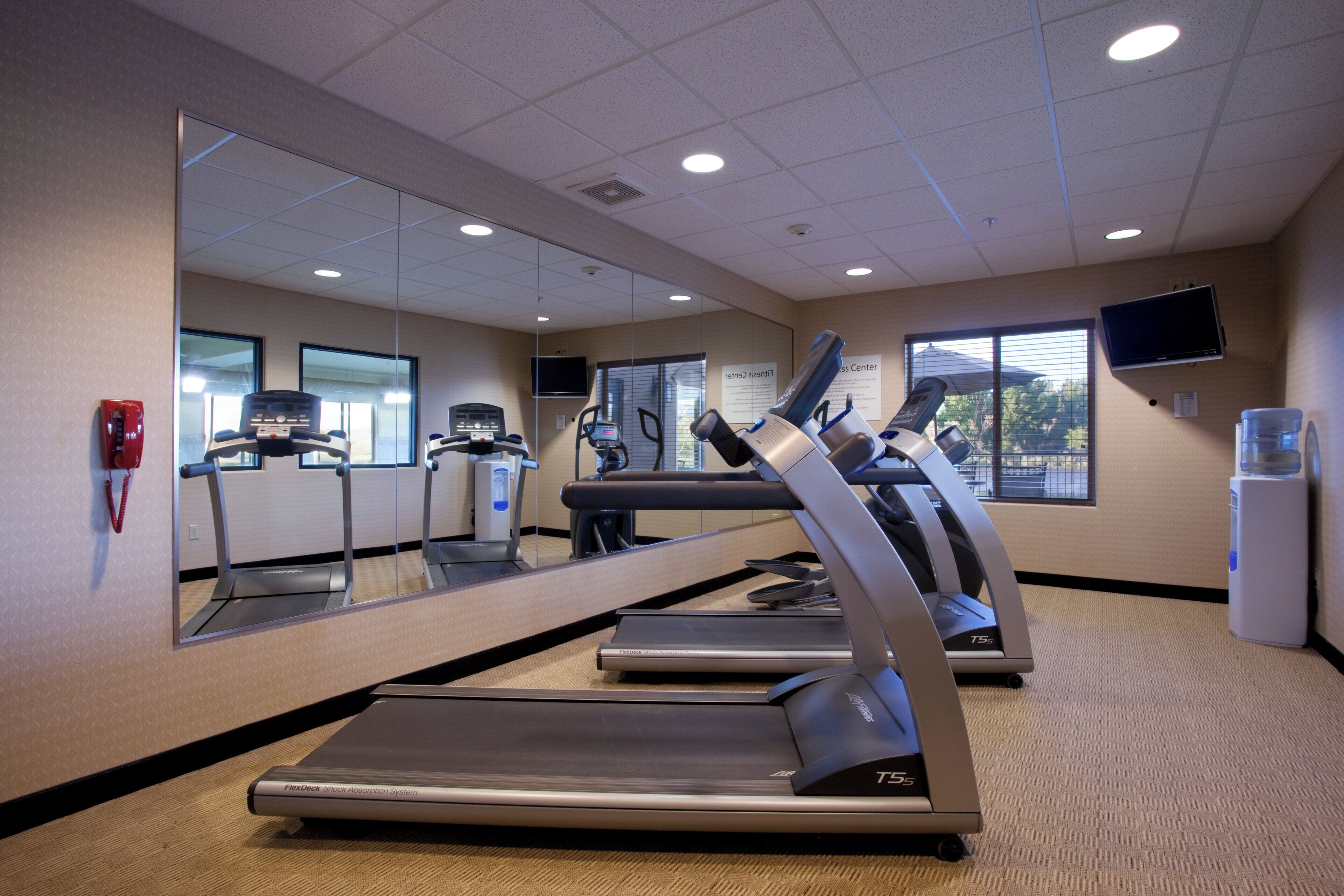 A fitness center with treadmills, a mirrored wall, and a television.
