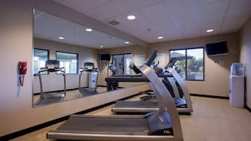 A fitness center with treadmills, a mirrored wall, and a television.