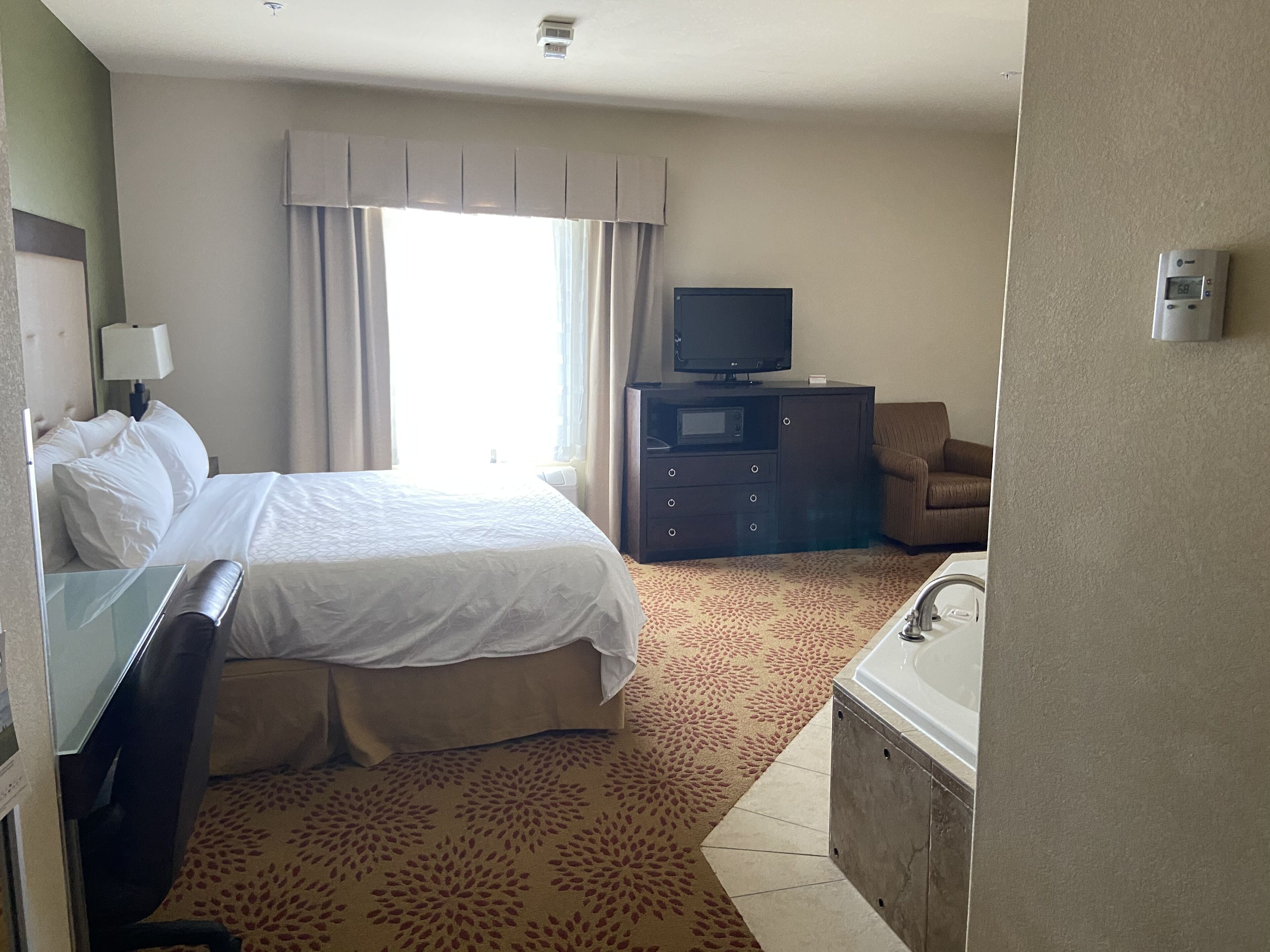 Hotelkamer met een bed, bureau, stoel, televisie, kast en badkamer met bad en wastafel.