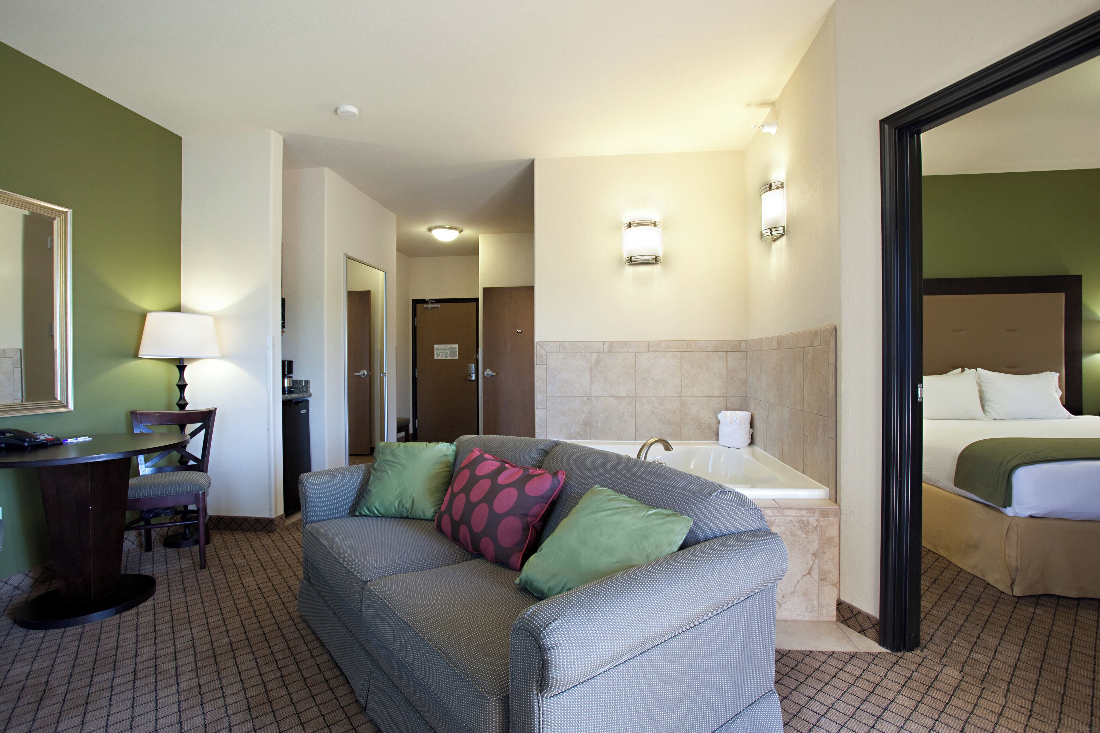 A hotel room with a sofa, a desk with a lamp, a bathroom with a bathtub, and a bed.