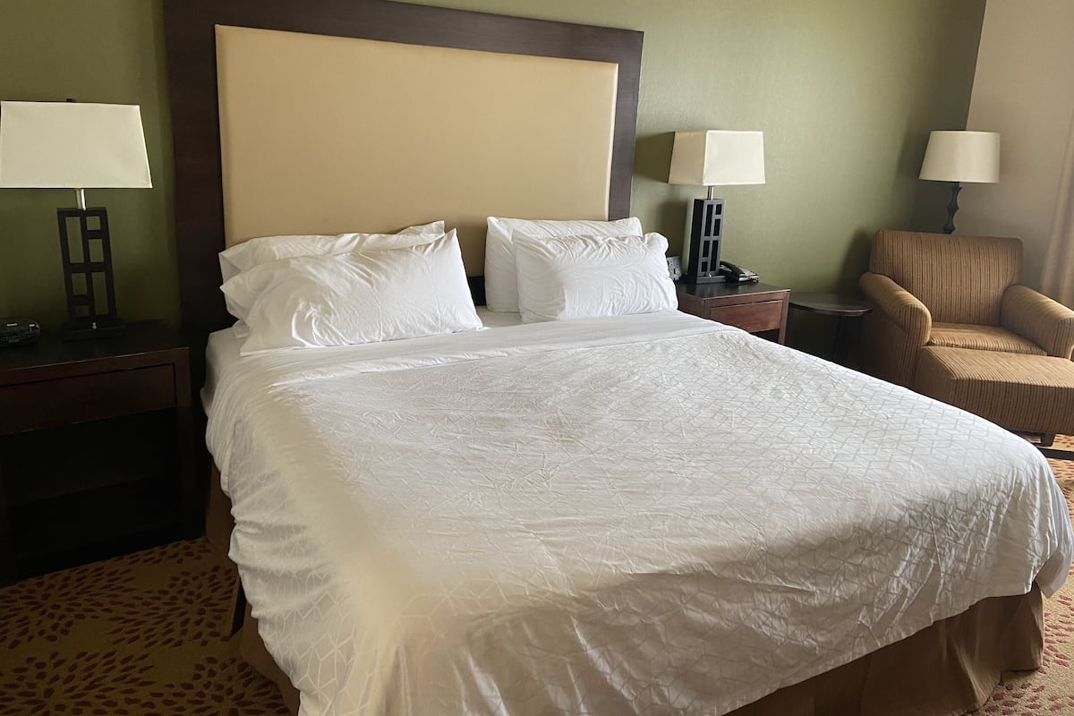 Ein Hotelzimmer mit einem großen Bett, zwei Nachttischen, zwei Lampen, einem Sessel und einem Beistelltisch.