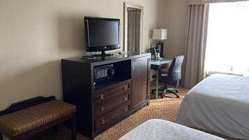 A hotel room with a bed, a desk with a chair, a television on a dresser, and a window with curtains.