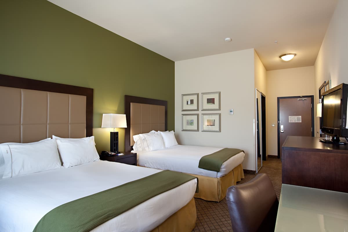 Ein Hotelzimmer mit zwei Betten, einem Schreibtisch, einem Sessel und einem Fernseher.