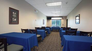 A conference room with multiple tables and chairs, a patterned carpet, and a framed picture on the wall.