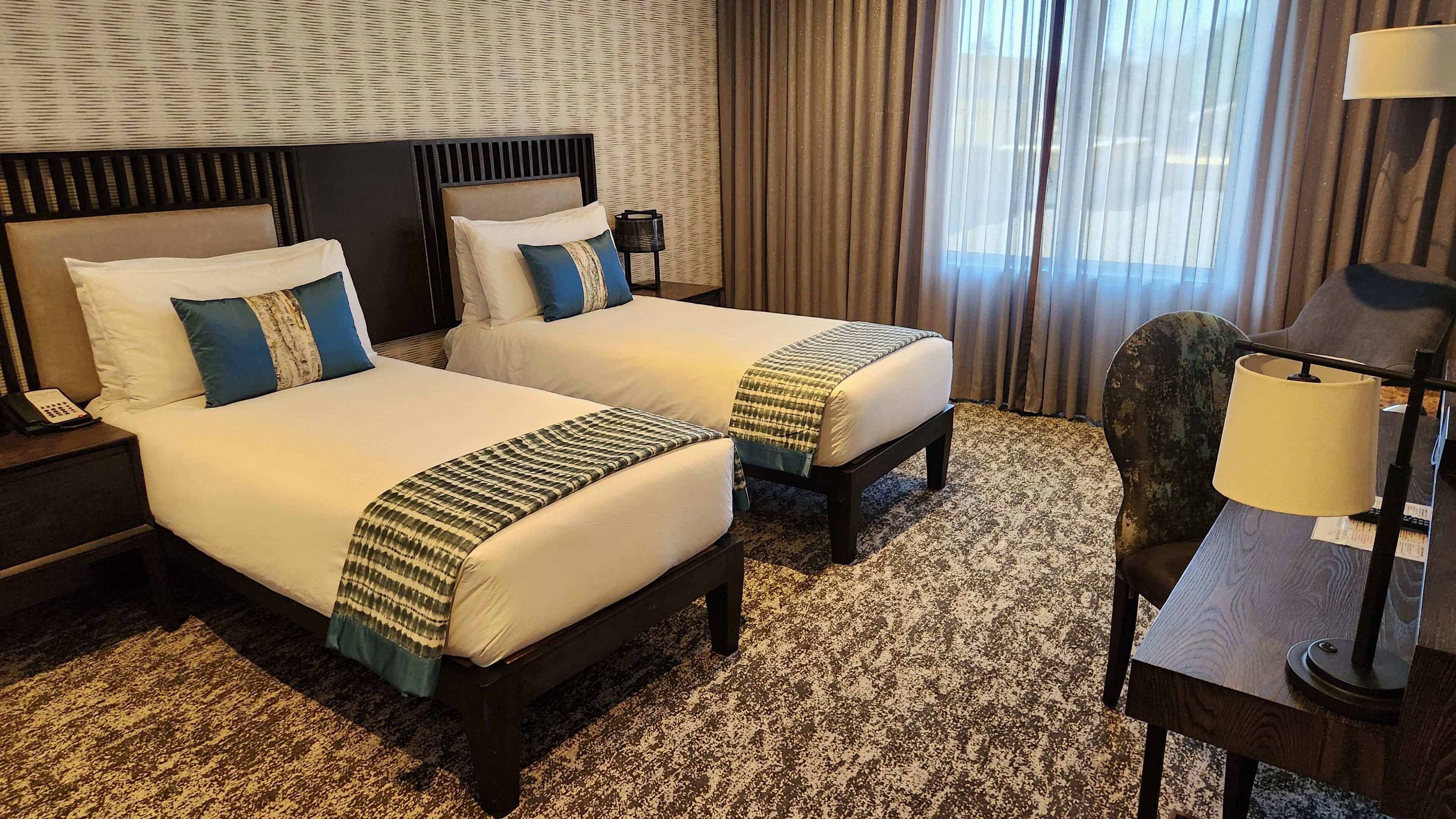 Habitación de hotel con dos camas, un escritorio, una silla, una lámpara y un teléfono en la mesita de noche.