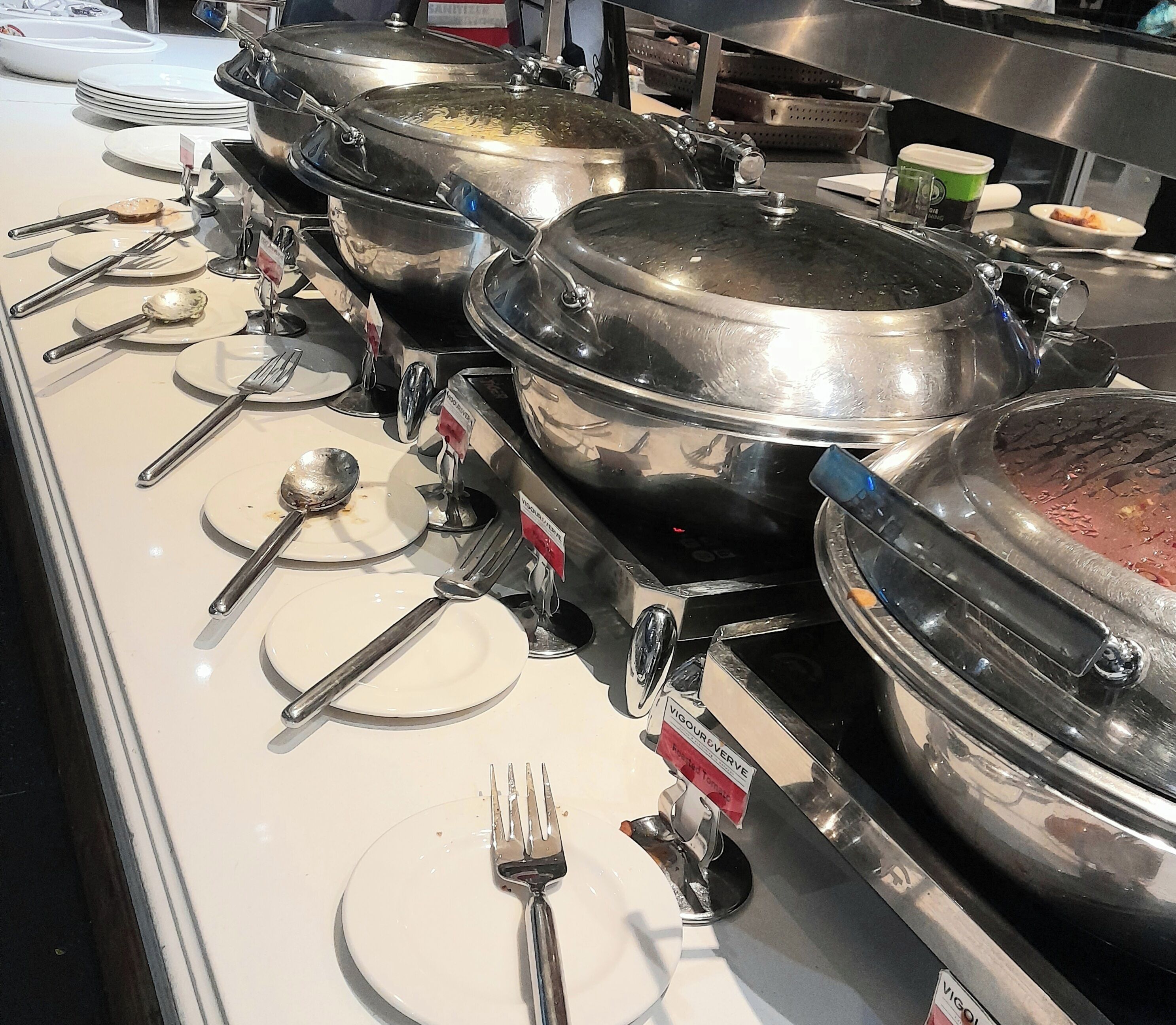 Montaje de bufé con múltiples estaciones de servicio, cada una con una olla grande, un plato y un tenedor.