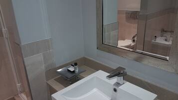 A modern bathroom with a white sink, a mirror, and a shower area.
