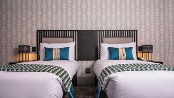 Habitación doble con dos camas, cada una con ropa de cama blanca y detalles azules, cabecero oscuro y pared con diseño.