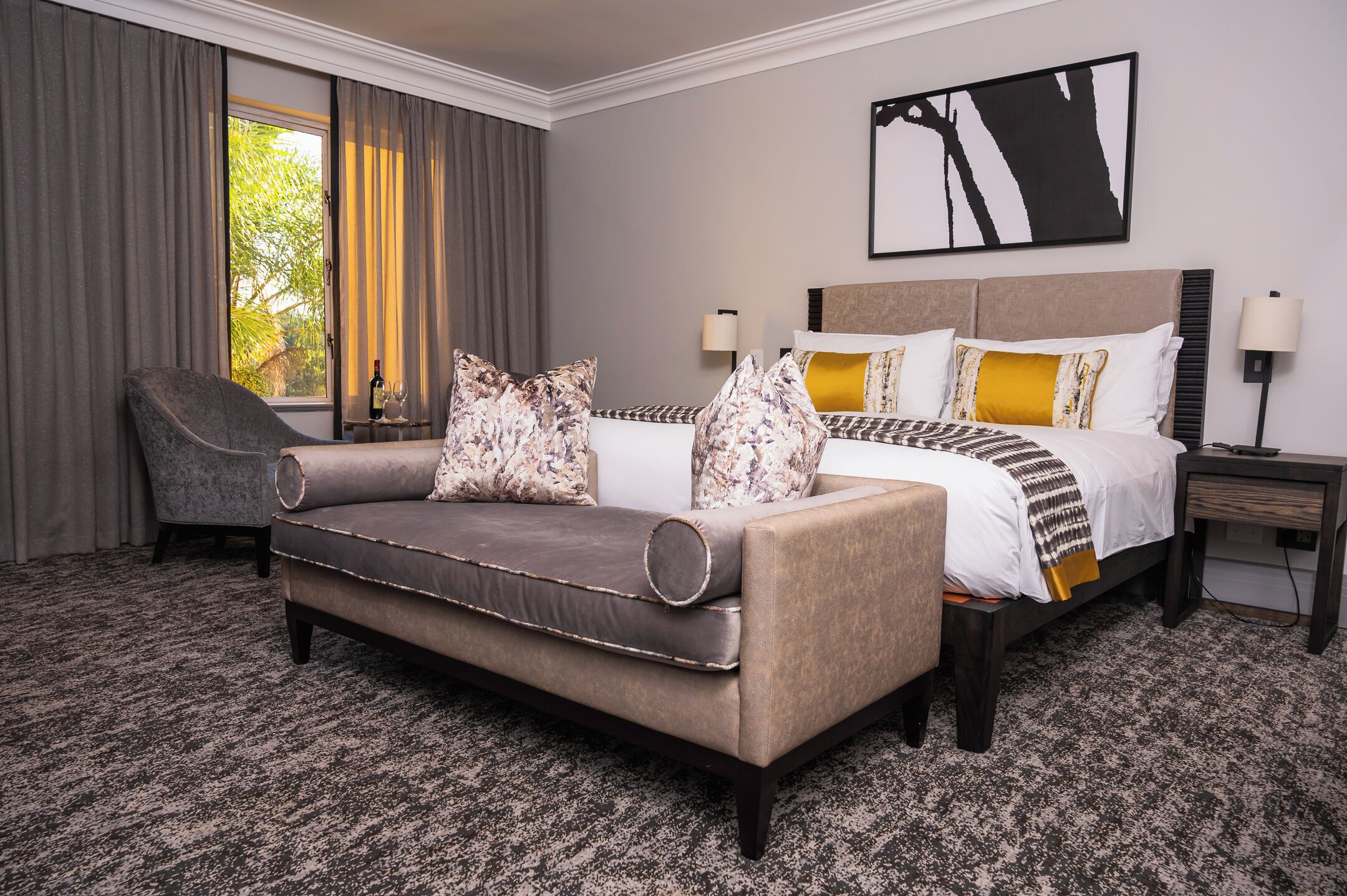 A hotel room with a sofa, a bed with patterned bedding, a chair, and a nightstand.