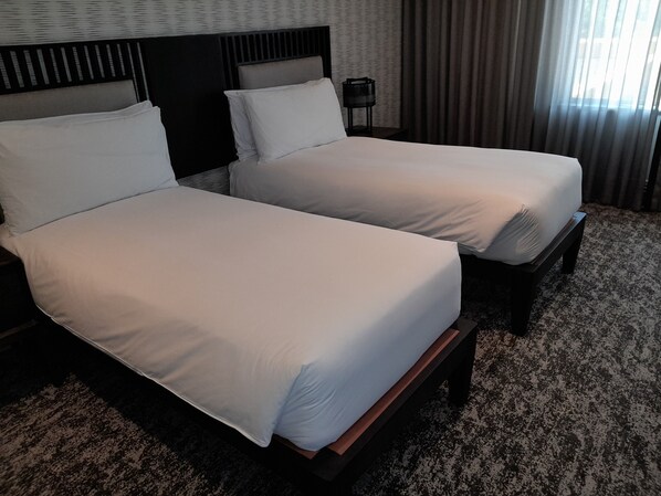 Une chambre d’hôtel avec deux lits simples, une tête de lit sombre, une petite table avec une lampe et une moquette à motifs.