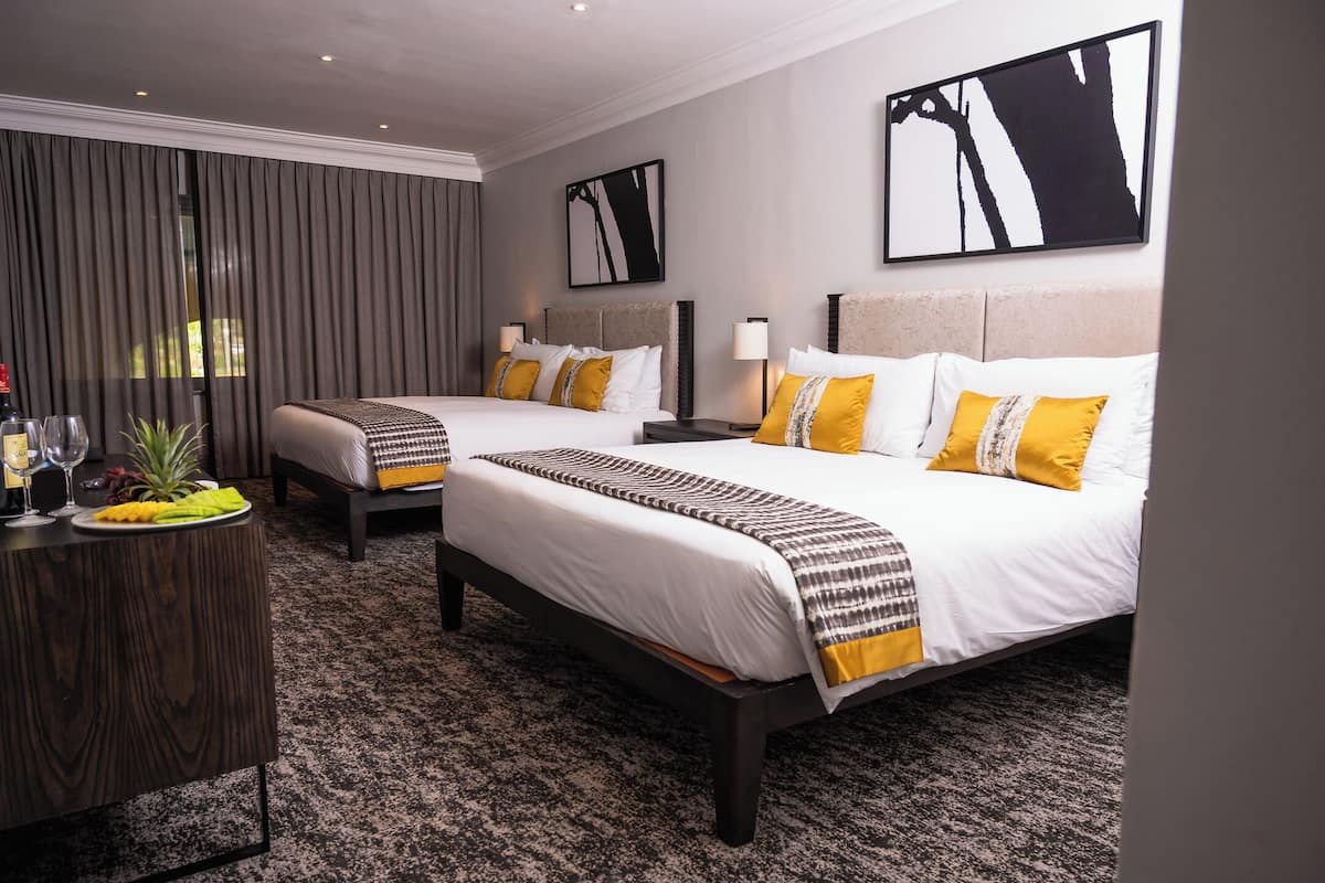 Una habitación de hotel con dos camas, una mesita de madera y un ventanal con cortinas.