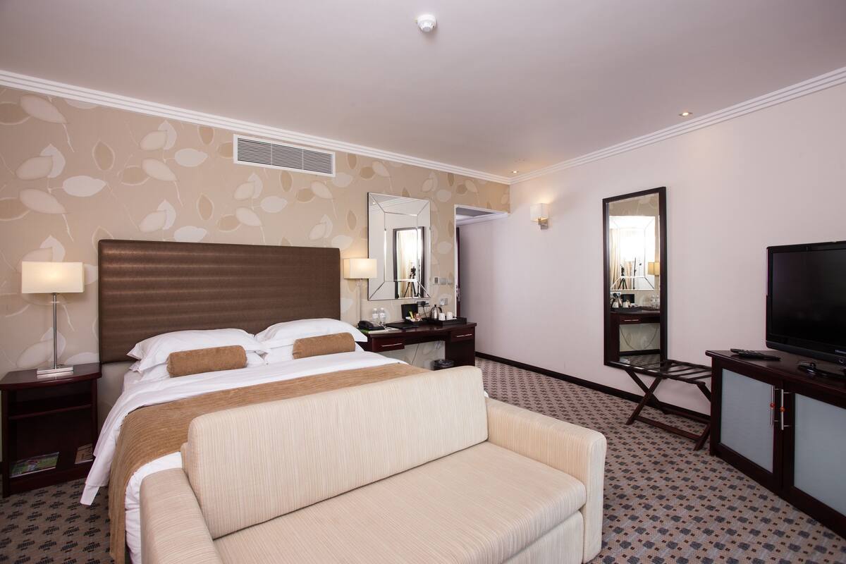 A hotel room with a large bed, a sofa, a TV, a desk, and a mirror.