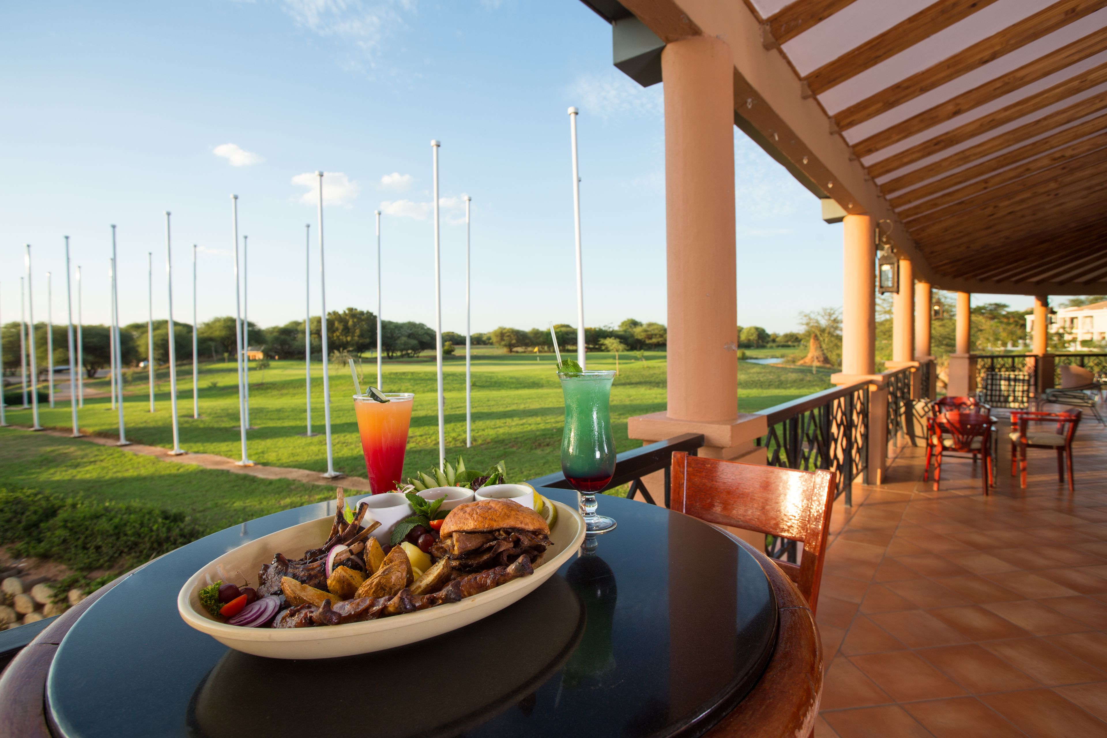 Ein Esstisch mit Speisen, einem Getränk und Blick auf einen Golfplatz.