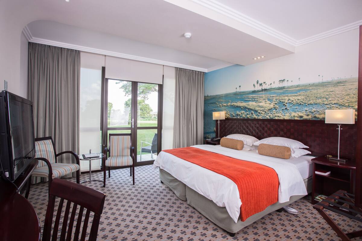 A hotel room with a large bed, a television, a seating area with chairs, and a view of a landscape through the window.