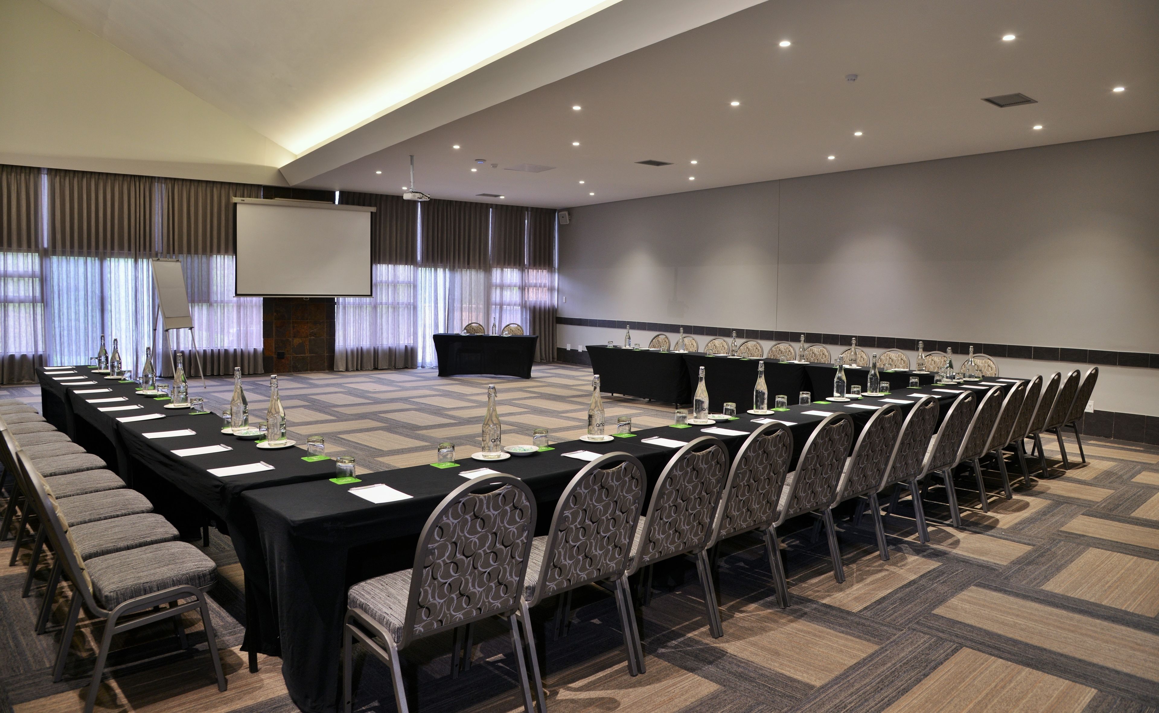 A conference room with a long table, chairs, a projector screen, and a stage.