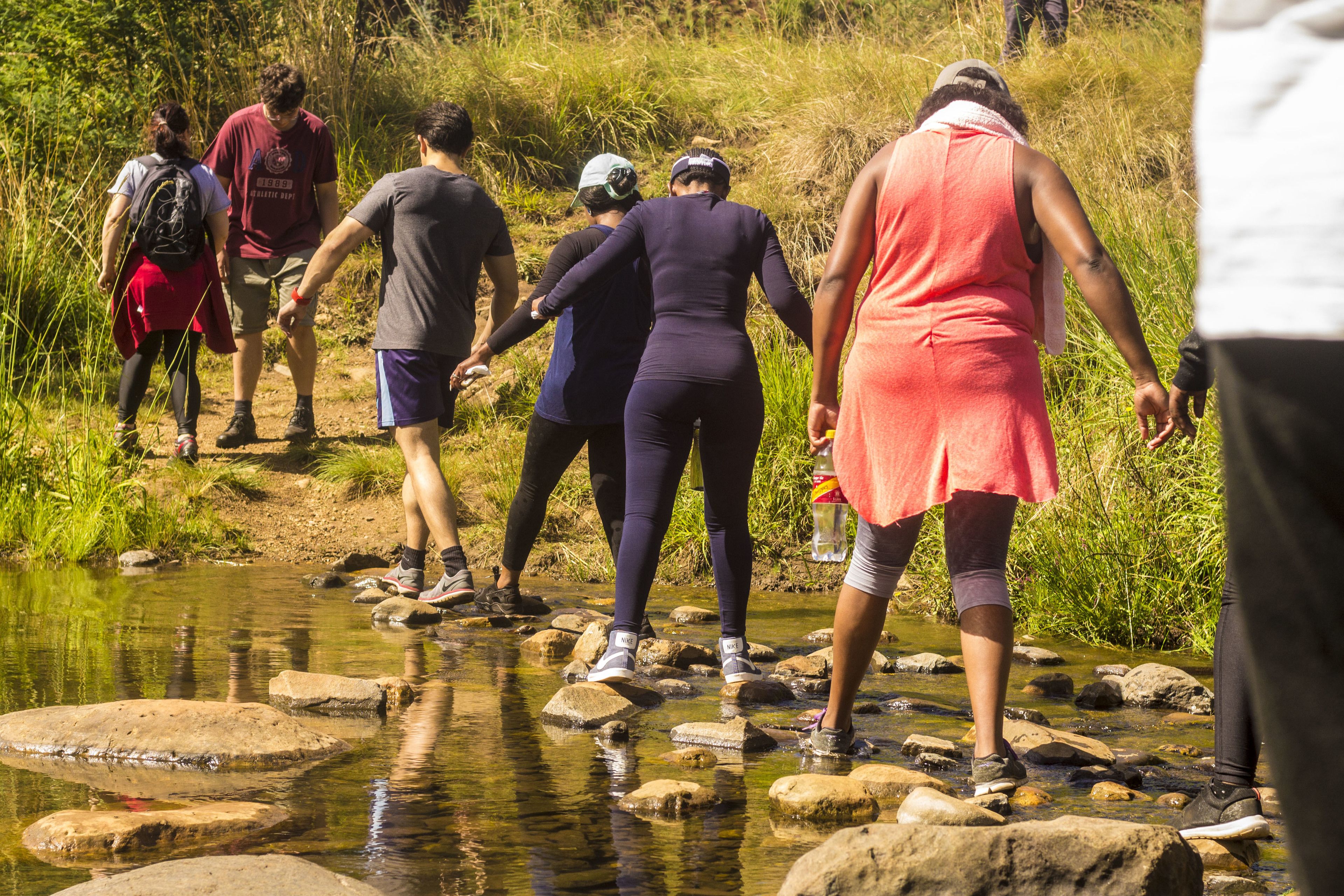 Des personnes traversent un petit ruisseau en marchant sur des rochers.