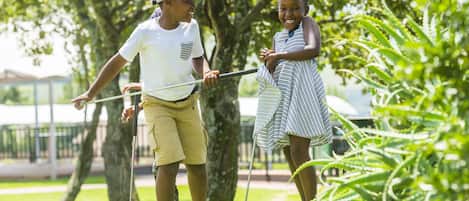 Two people playing golf on a green with trees in the background.