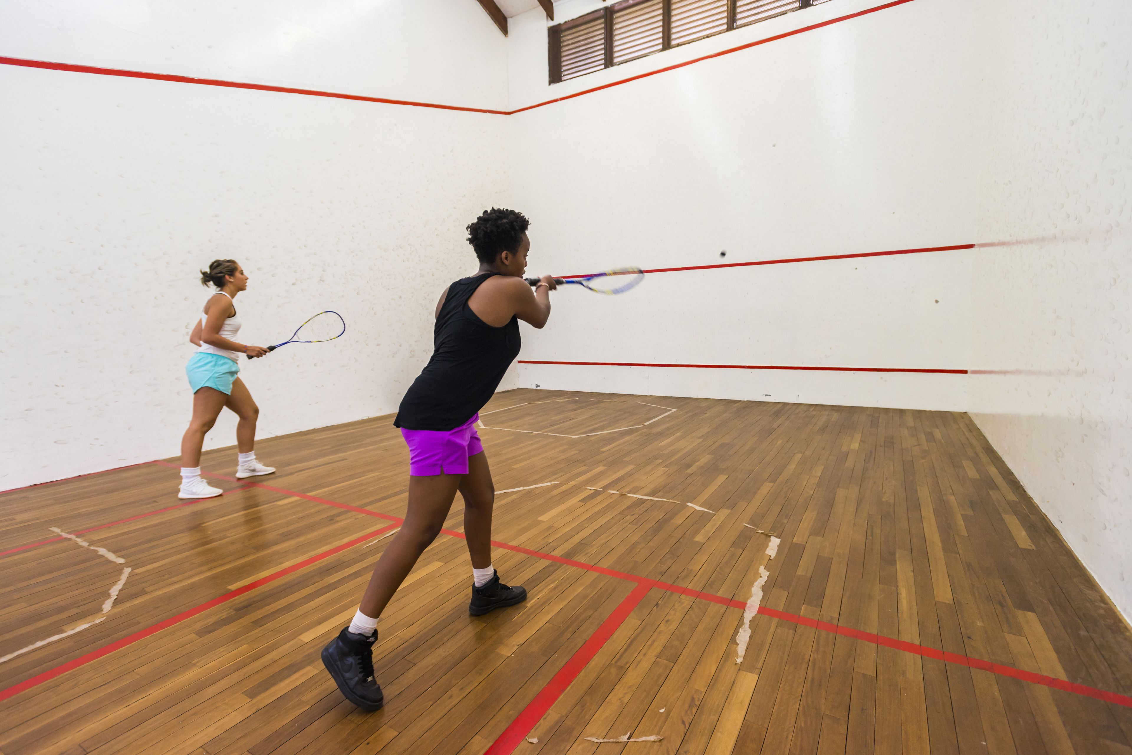 Una cancha de squash con suelo de madera y líneas delimitadoras rojas.