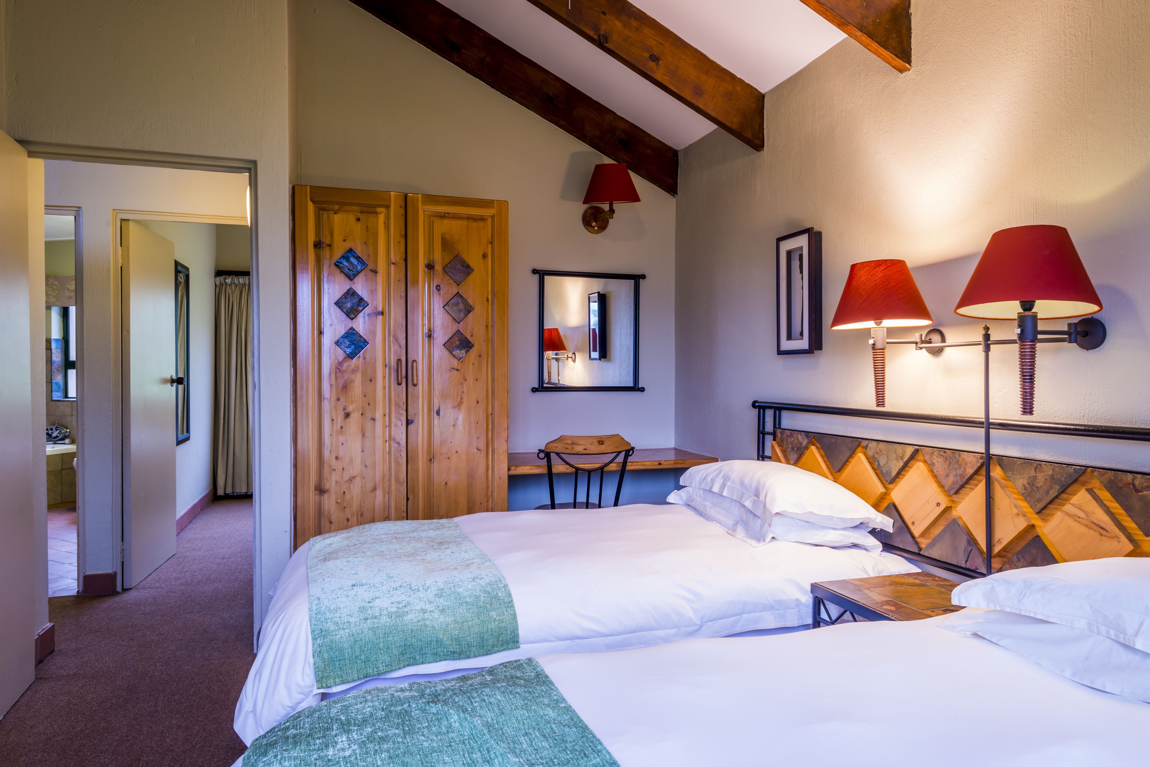 Een hotelkamer met twee bedden, een houten garderobe, een bureau en een stoel.