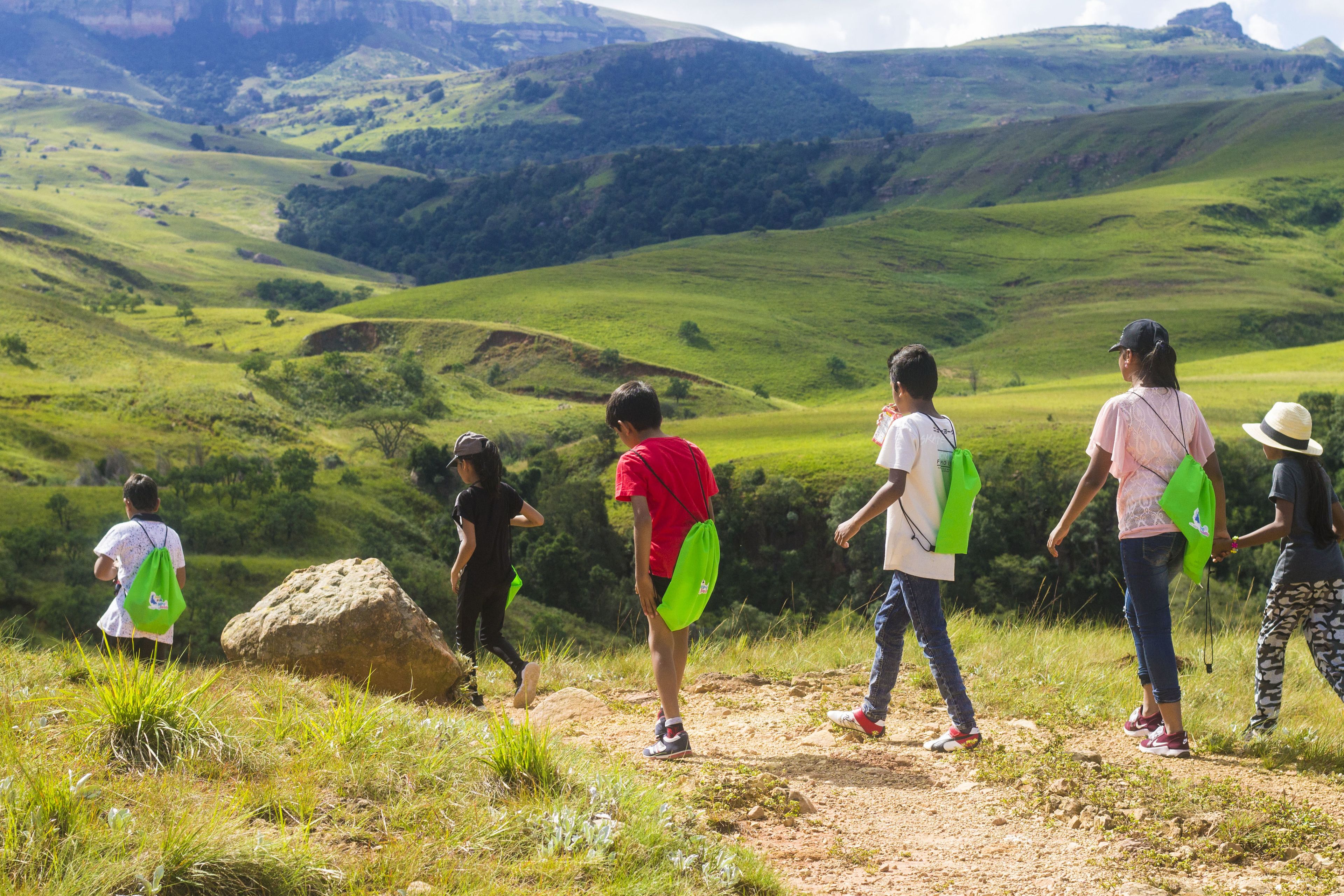 A group of people walking on a dirt path in a hilly landscape.