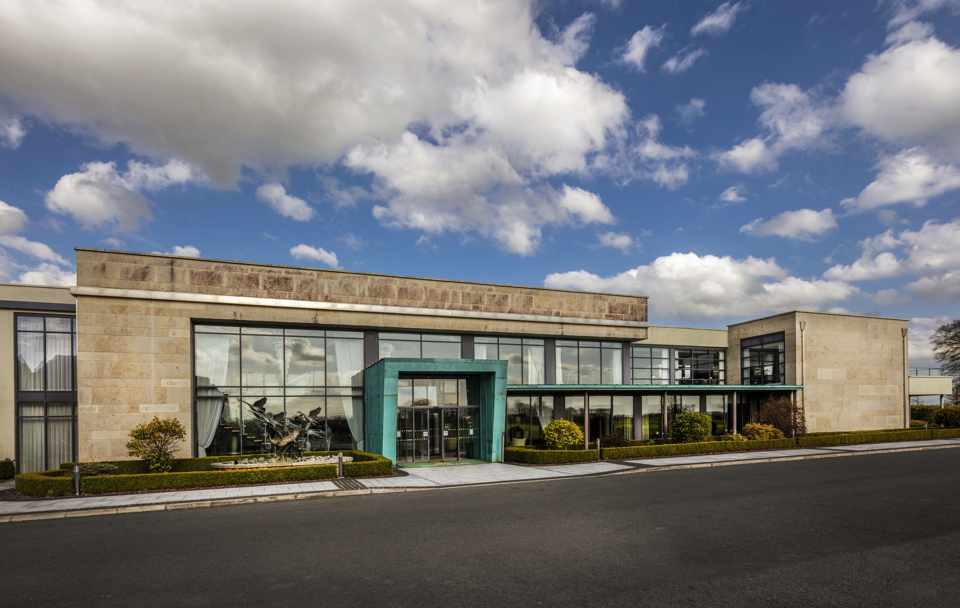 A modern building with large glass windows, a green entrance, and a well-maintained lawn.