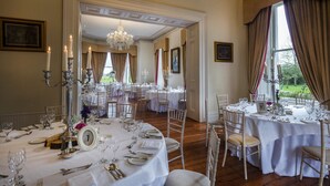 Un comedor formal con mesas redondas dispuestas para una comida, candelabros y vistas al exterior.