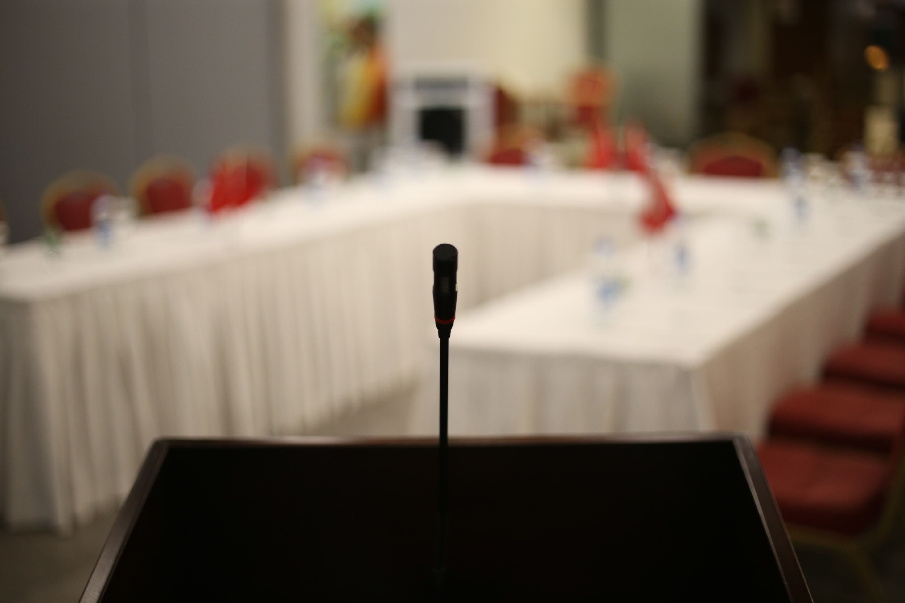 A conference room with a podium in the foreground and a blurred background of tables and chairs.