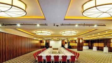 Un salón de conferencias con una larga mesa, sillas rojas y una alfombra estampada.