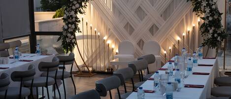 A banquet hall with tables set for a formal event, featuring white tablecloths, water bottles, and candles.