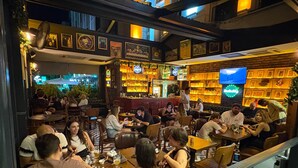 A restaurant with multiple tables and chairs, a bar area with shelves of bottles, and a television screen. - CK Farabi Hotel (Ankara)