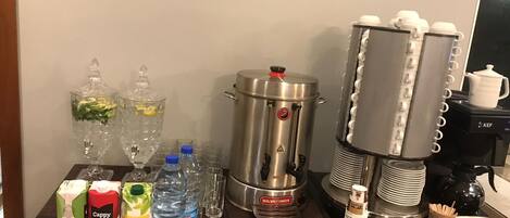 A coffee station with a coffee maker, a milk frother, and various coffee cups and mugs.