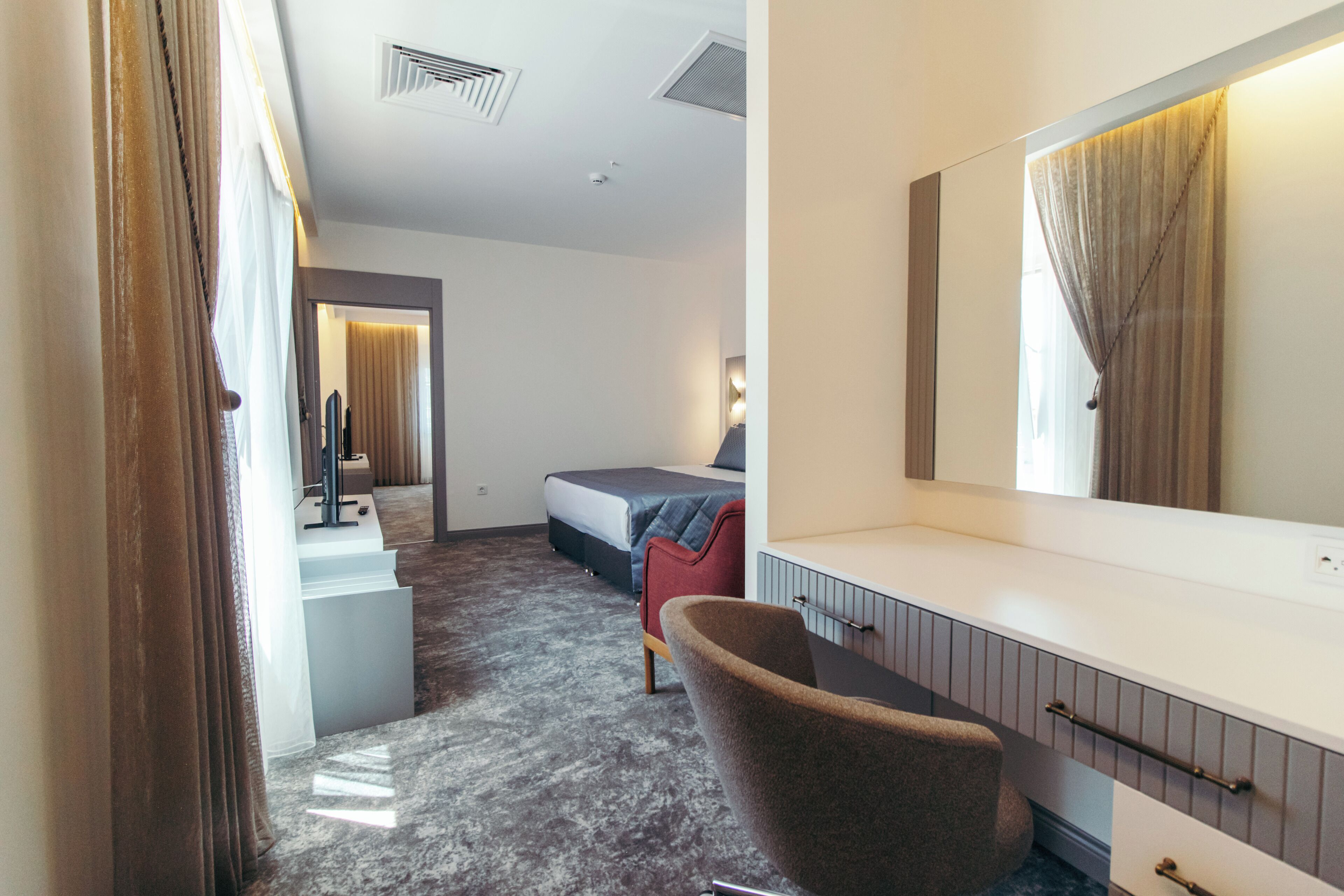 A hotel room with a bed, a chair, a desk, and a large mirror.