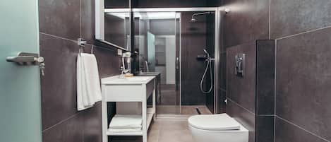 Un baño moderno con inodoro blanco, lavabo con espejo y zona de ducha.