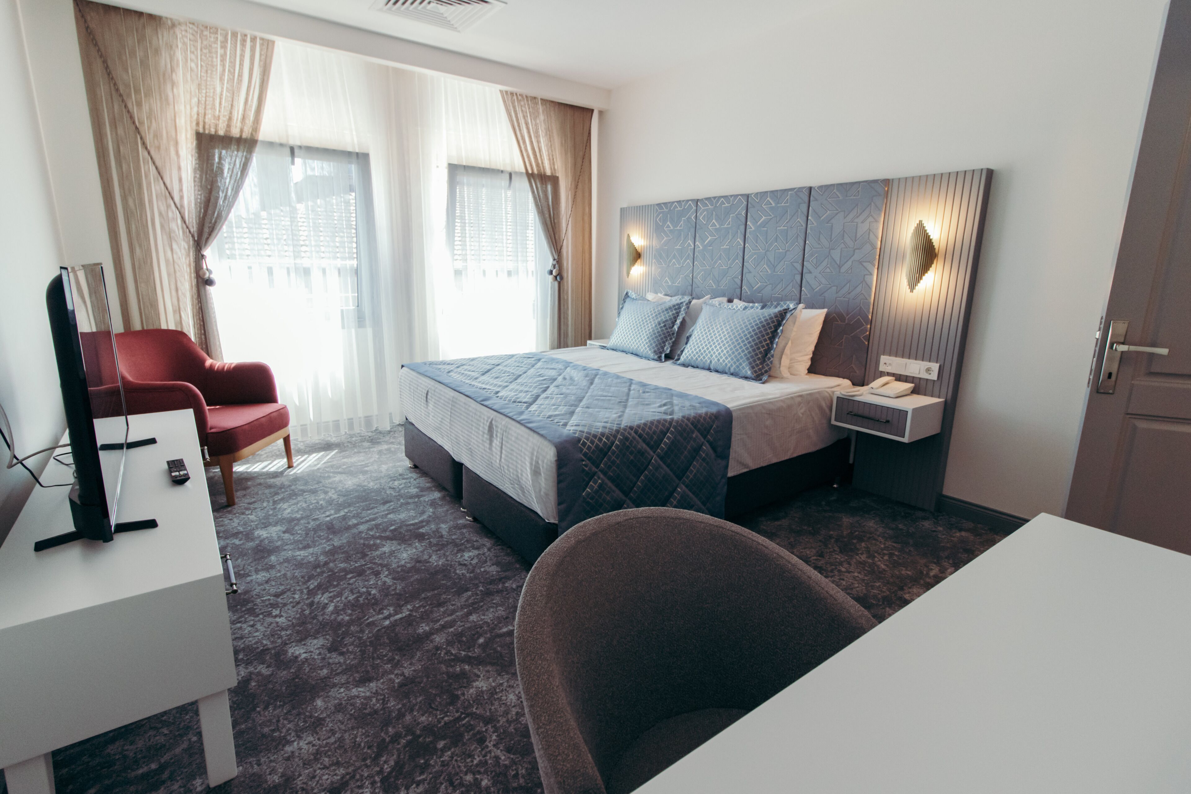 Et moderne hotelværelse med en stor seng, et skrivebord, en stol og et fjernsyn.