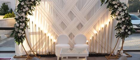 A rooftop terrace with a white draped backdrop, two white chairs, a small table, and candle holders.