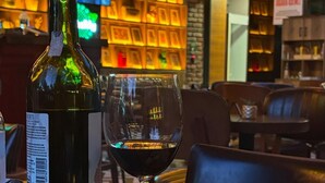 A bottle of wine, a glass, and a cheese board with various cheeses and fruits on a table in a restaurant. - CK Farabi Hotel (Ankara)