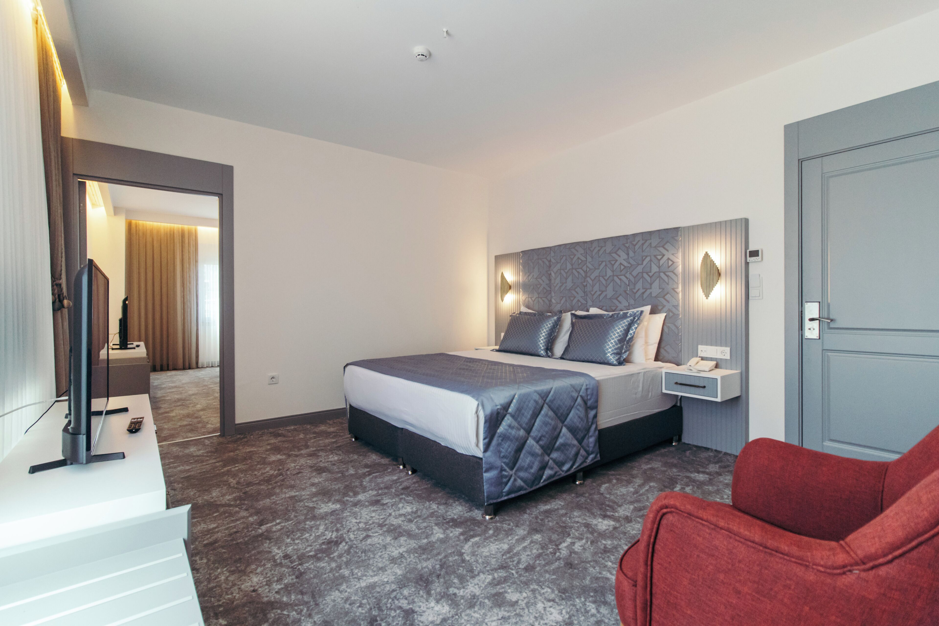 Una habitación de hotel moderna con una cama grande, una mesita de noche y un sillón rojo.