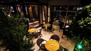 An outdoor seating area with round tables and wicker chairs, surrounded by greenery. - CK Farabi Hotel (Ankara)
